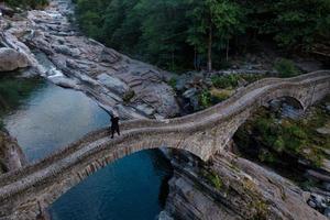 An old arched stone bridge over a stream with a person standing on it. photo