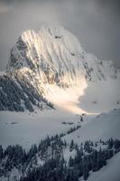 A mountain covered with snow on which the sunlight falls next to a house stands photo