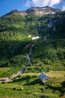 A waterfall running down the mountain in the valley is a small hut photo