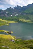 a chapel standing by a lake surrounded by mountains photo