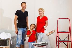 The young joyful family does repair at home, they paint the wall with help of platens photo