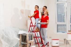 Happy family mother father and child daughter are doing repairs paint wall at home photo