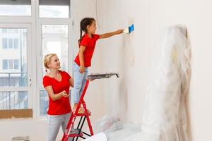 Happy family mother and child daughter making repairs, paint the wall at home photo