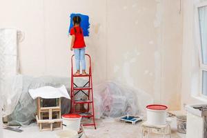 Repair in the apartment. Happy child girl paints the wall with blue paint photo