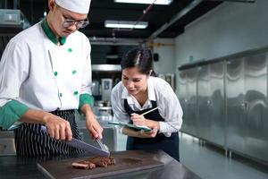 Student cooking apprentice Take notes on every step as the chef cooks in the culinary academy's kitchen. photo