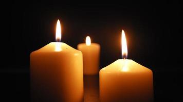 três velas queimam com uma chama amarela suave no escuro e são apagadas pelo vento. câmera lenta.
