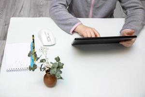 tablet in the hands of a child sitting at a white table, copy space, online learning photo