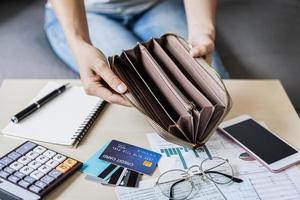 una joven estresada abre su billetera vacía y calcula los gastos en casa