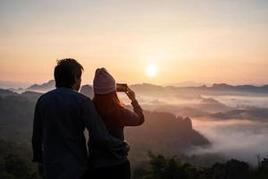 joven pareja viajera mirando el mar de niebla y la puesta de sol sobre la montaña en mae hong son, tailandia foto