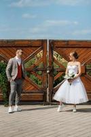 young couple bride in a white short dress and groom in a gray suit near the wooden gate photo