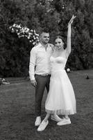 the first dance of the groom and bride in a short wedding dress on a green meadow photo