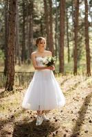 young bride in a white short dress in a spring pine forest photo