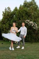 the first dance of the groom and bride in a short wedding dress on a green meadow photo