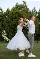 the first dance of the groom and bride in a short wedding dress on a green meadow photo