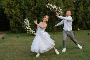 the first dance of the groom and bride in a short wedding dress on a green meadow photo