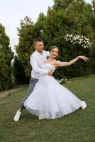 the first dance of the groom and bride in a short wedding dress on a green meadow photo