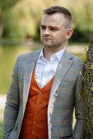 portrait of the groom in a gray suit and an orange vest photo