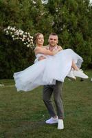 the first dance of the groom and bride in a short wedding dress on a green meadow photo