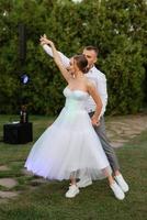 the first dance of the groom and bride in a short wedding dress on a green meadow photo