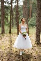 young bride in a white short dress in a spring pine forest photo