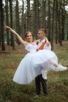 young couple bride in a white short dress and groom in a gray suit in a pine forest photo