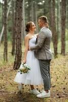 joven Pareja novia en un blanco corto vestir y novio en un gris traje en un pino bosque foto