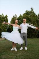 the first dance of the groom and bride in a short wedding dress on a green meadow photo