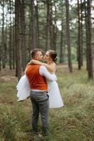 joven Pareja novia en un blanco corto vestir y novio en un gris traje en un pino bosque foto