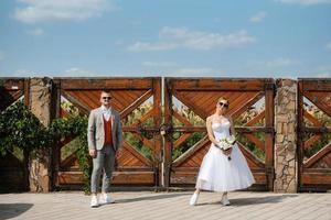 joven Pareja novia en un blanco corto vestir y novio en un gris traje cerca el de madera portón foto