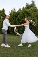 the first dance of the groom and bride in a short wedding dress on a green meadow photo