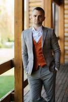 portrait of the groom in a gray suit and an orange vest photo