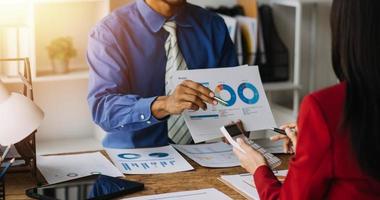 Group of confident business people point to graphs and charts to analyze market data, balance sheet, account, net profit to plan new sales strategies to increase production capacity. photo