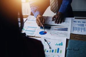 Group of confident business people point to graphs and charts to analyze market data, balance sheet, account, net profit to plan new sales strategies to increase production capacity. photo