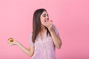 Beauty model girl eating colorful donuts. Funny joyful styled woman choosing sweets on pink background. Diet, dieting concept. Junk food, Slimming, weight loss photo