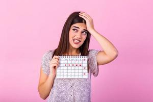 joven hermosa mujer participación menstruación calendario terminado aislado antecedentes con sorpresa rostro. joven niña participación menstruación calendario con confuso rostro, temeroso y emocionado con temor expresión foto