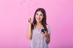 hermosa joven mujer en auriculares escuchando a música sonriente con música notas en pie en un rosado antecedentes. sensación aumentar de felicidad desde escuchando genial canciones en auriculares. foto