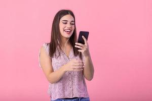Excited beautiful girl hold mobile phone with headphones listening to music on blank empty screen isolated on pink studio background . Emotions, lifestyle concept. Copy space.
