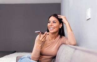Woman laughing while talking on speakerphone. technology, communication and people concept - happy woman using voice command recorder on smartphone photo