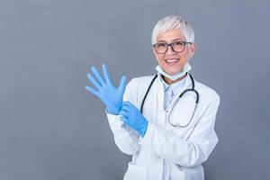 Senior female Doctor putting on protective gloves, isolated on background. Doctor putting on sterile gloves photo