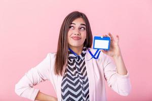 Beautiful success woman shows on camera her badge and smiling over pink wall. Young attractive woman holding blank artist lanyard or badge in hand with metal piece. Plastic pass concept. photo