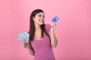 Beautiful young casual blonde girl standing isolated over pink background, showing plastic credit card and money banknotes photo