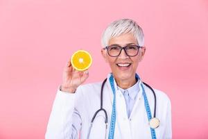 Smiling nutritionist holding a sliced orange, vitamins and healthy diet concept. Nutritionist with healthy fruit, juice and measuring tape. Dietitian working on diet plan. photo