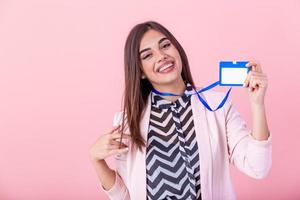 Beautiful success woman shows on camera her badge and smiling over pink wall. Young attractive woman holding blank artist lanyard or badge in hand with metal piece. Plastic pass concept. photo