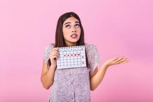 Portrait of young woman in dress, holding female periods calendar for checking menstruation days isolated on trending pink background. Medical healthcare, gynecological concept. photo