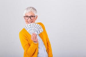 Closeup portrait super happy excited successful senior woman pensioner holding money dollar bills in hand. Positive emotion facial expression feeling. online shopping photo