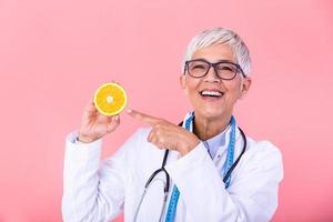 Middle aged nutritionist woman holding orange fruit happy with big smile and finger pointing to the fruit, Nutritionist with healthy fruit, juice and measuring tape. Dietitian working on diet plan. photo