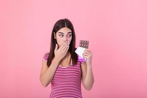 Portrait of a happy young woman with chocolate bar isolated over pink background covenring her mouth. Young woman with natural make up having fun and eating chocolate isolated on pink background photo