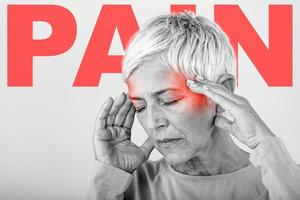 Woman suffering from stress or a headache grimacing in pain. Senior woman with migraine feeling unwell. Portrait of an attractive senior woman with a headache, feeling pain photo