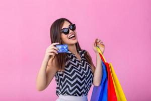 hermosa joven mujer con compras pantalones participación su crédito tarjeta en rosado fondo.shopaholic compras moda. foto