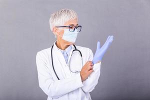 Senior female Doctor putting on protective gloves and mask, isolated on background. Doctor putting on sterile gloves photo